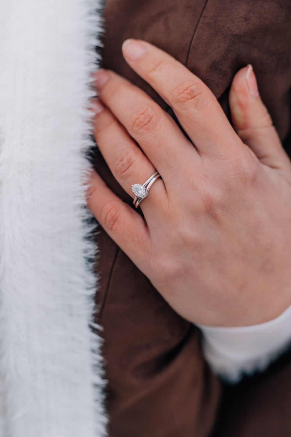 Close-up of an engagement ring against white fur and brown fabric.