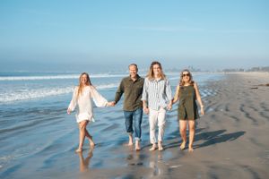 Family of four waling down beach next to ocean in Coronado CA