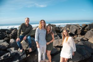 Family of four smiling and posing on rocks in Coronado CA on beach