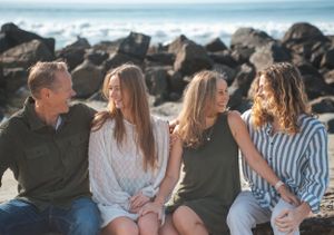 Family of four smiling on beach in Coronado CA in front of rocks