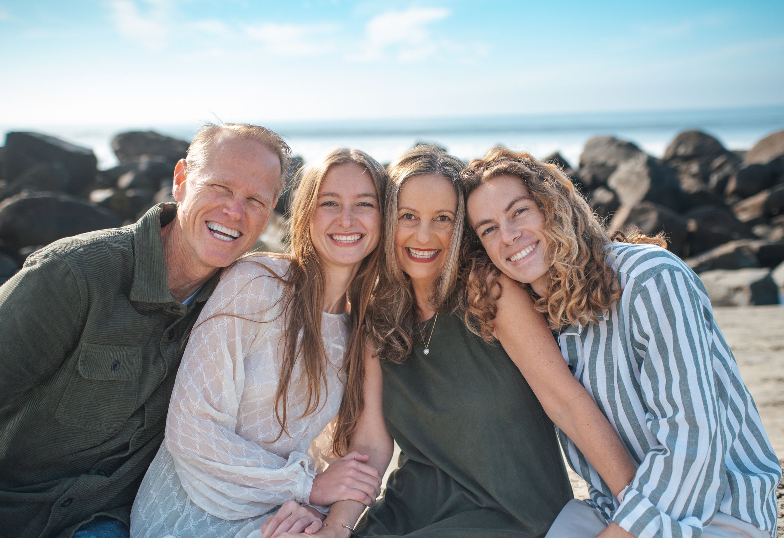 Family of four smiling on beach in Coronado CA in front of rocks