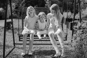 Three people sit together on an outdoor garden swing in black and white photography.