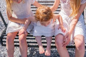 People in white lace dresses sit together on a striped outdoor swing in summer.