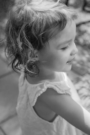 Black and white portrait of a young child wearing a white dress looking to the side with curly hair.