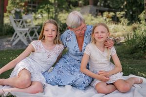 Three people sitting together on white blanket in garden wearing light summer dresses.