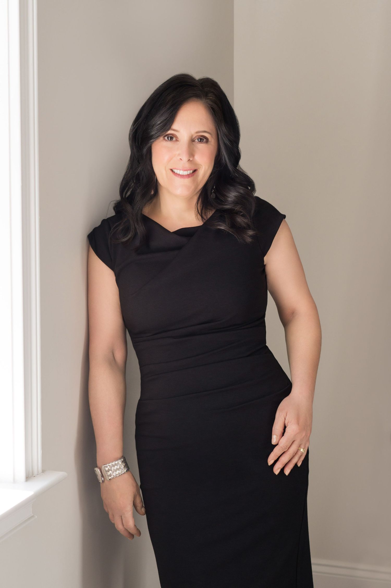 Professional portrait of someone wearing an elegant black dress standing next to a window in natural lighting. branding
