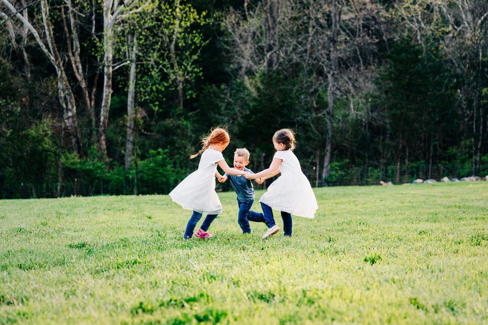 Picture of 3 young children playing ring around the rosie in a field by Dandridge family and children photographer