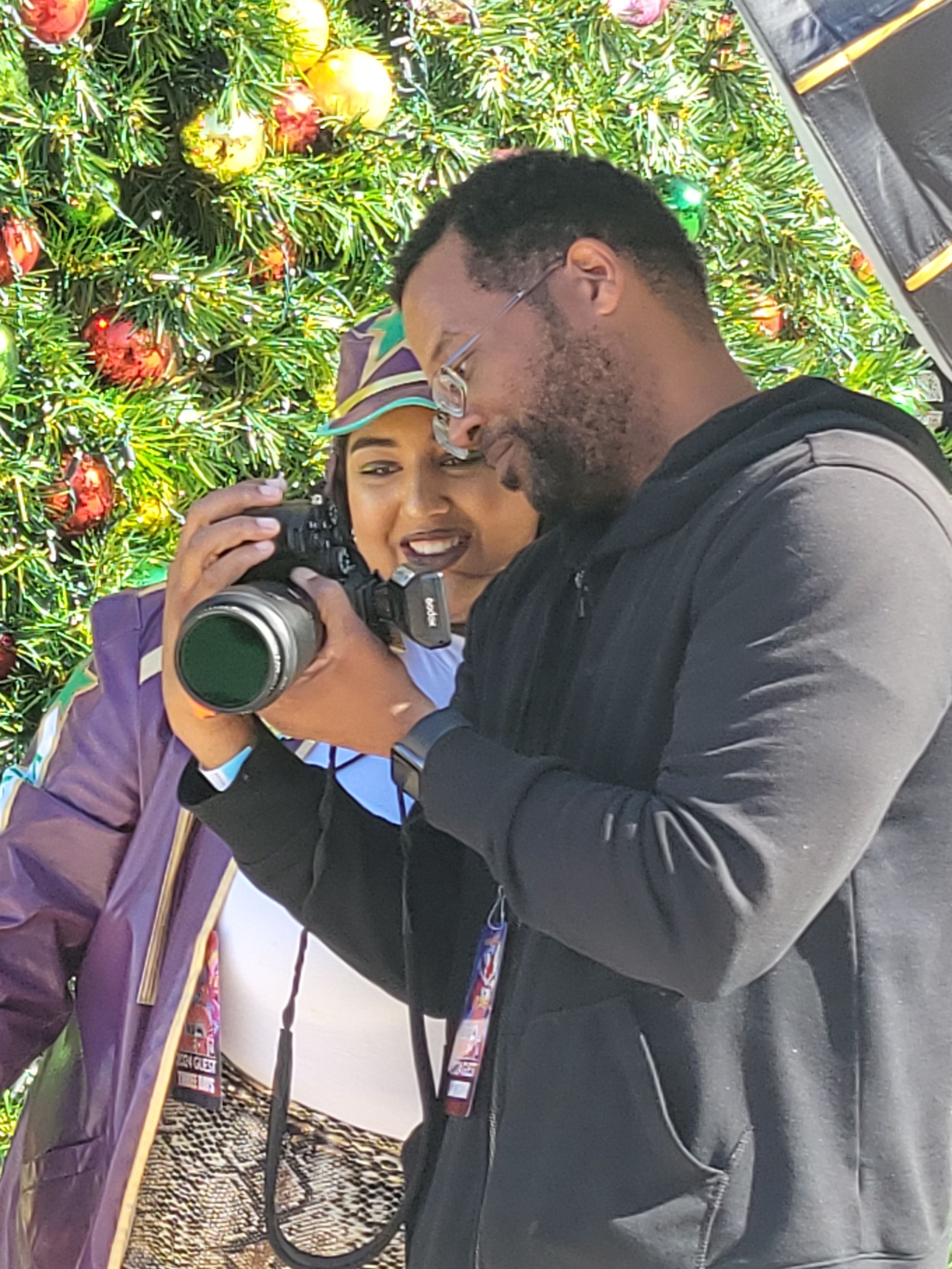 Two photographers examining photos together under festive Christmas tree decorations.