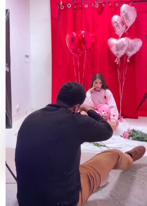 Behind-the-scenes Valentine's Day photoshoot with heart balloons and red backdrop.