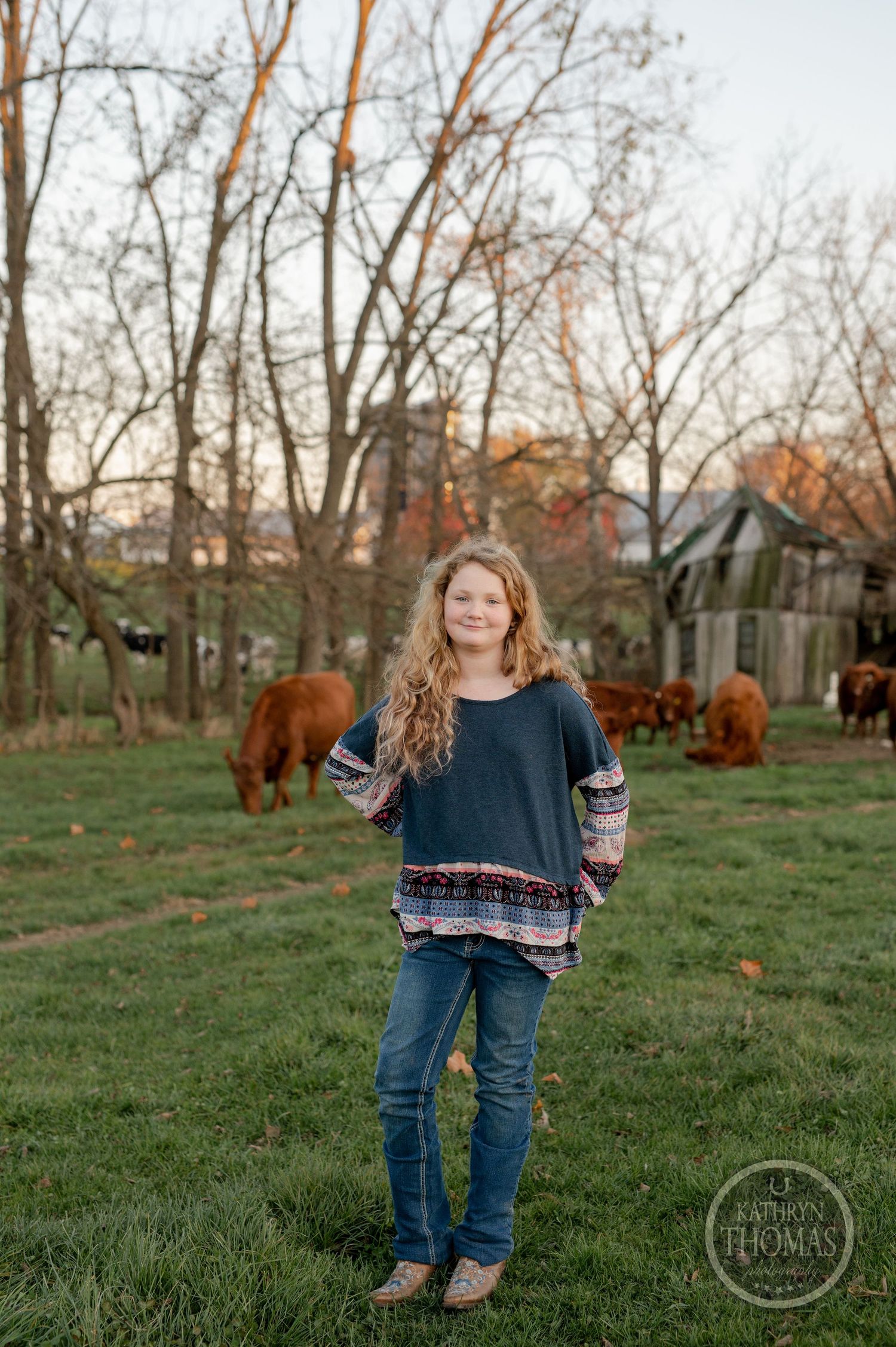 A casual outdoor portrait in a field with grazing Highland cattle and bare trees in the background.