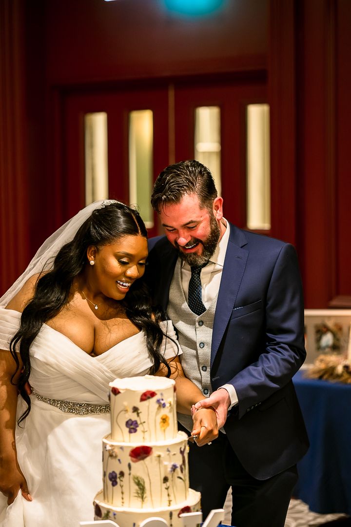 A joyful wedding cake cutting moment captured in warm lighting.