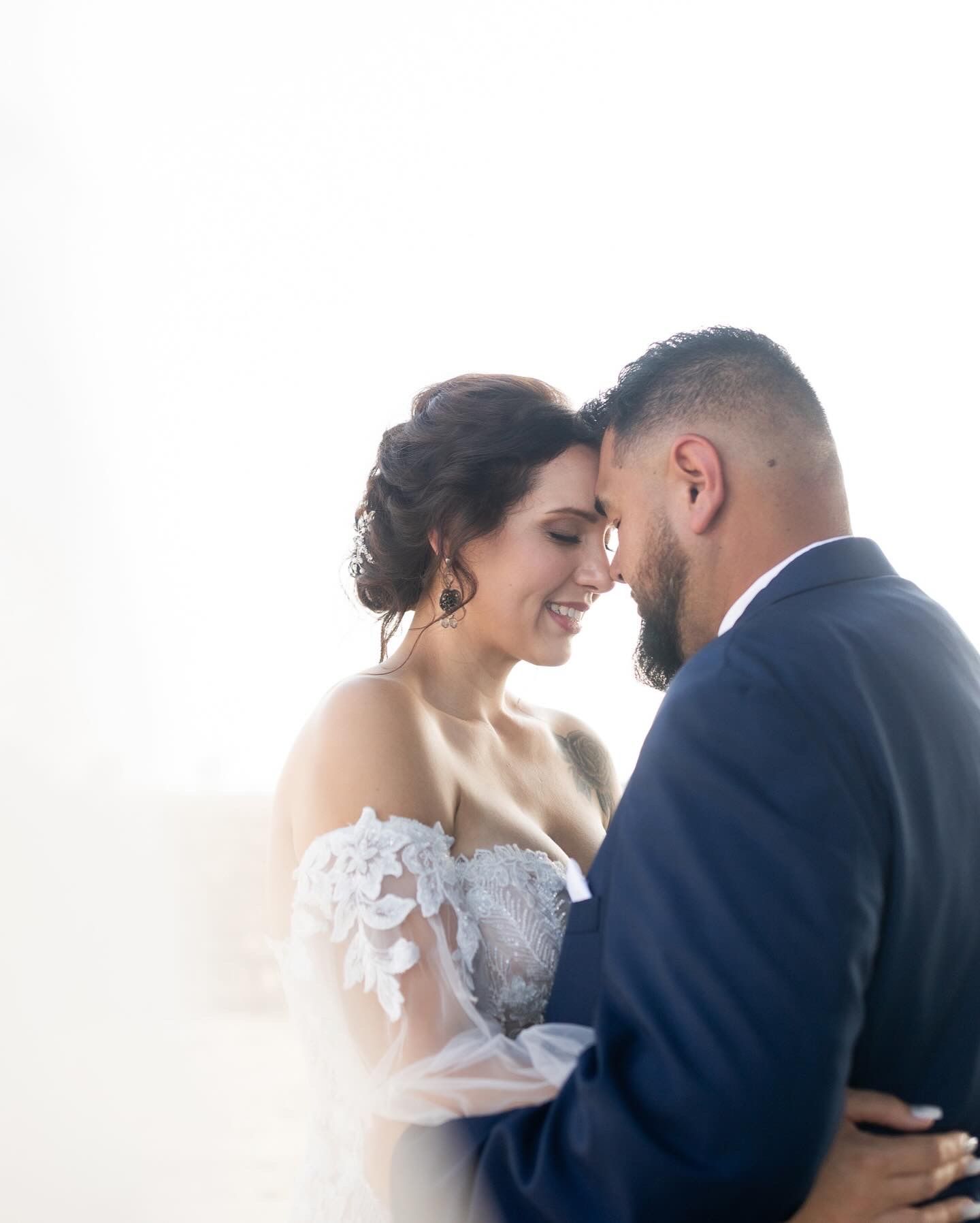 Intimate wedding portrait of couple in formal attire against bright background.