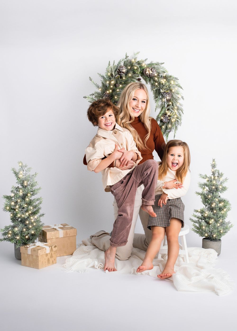 Festive family photo with holiday decorations including wreath, trees and wrapped gifts.