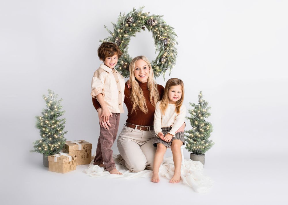 Family holiday portrait with Christmas wreath, mini trees and wrapped presents on white background.