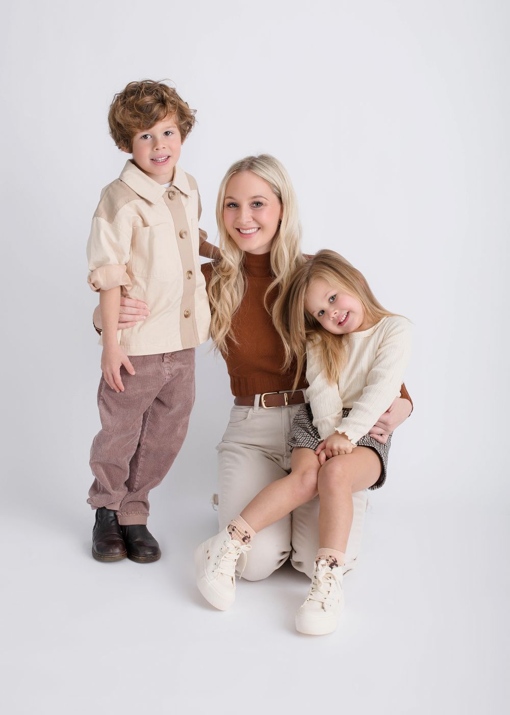 Portrait of a family in coordinating neutral outfits posing against a white backdrop.