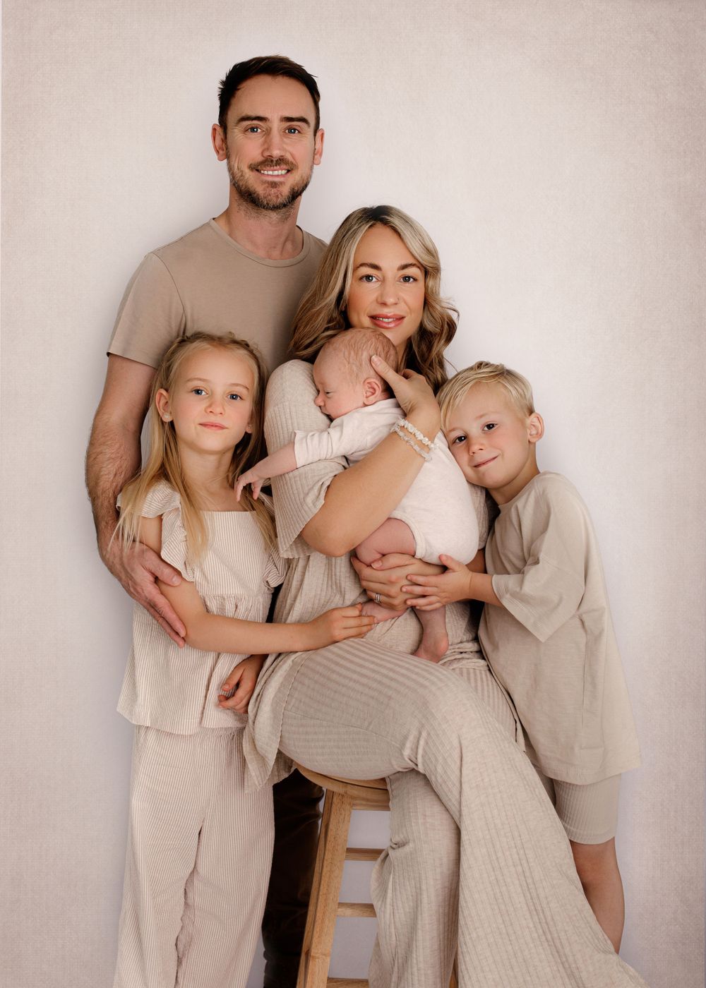Family of five in coordinated beige and neutral outfits pose together against plain background.