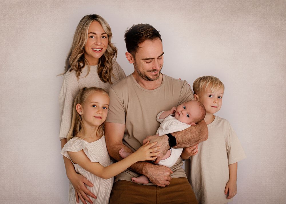 Candid family portrait with everyone wearing coordinated neutral colors against beige wall.