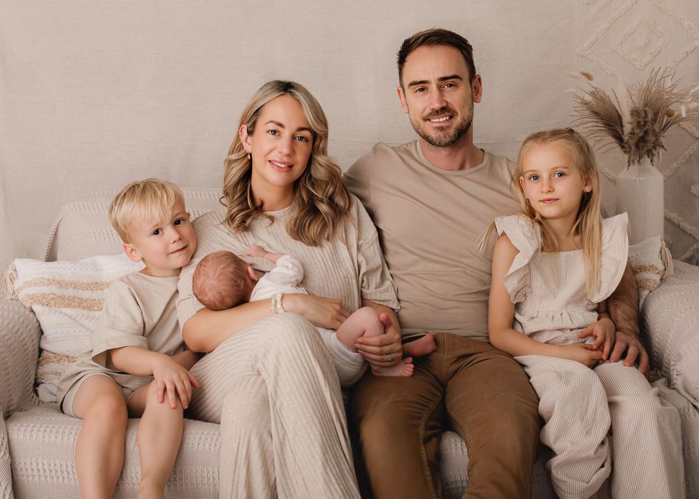 Family sitting together on couch in coordinated beige and neutral tones for portrait session.