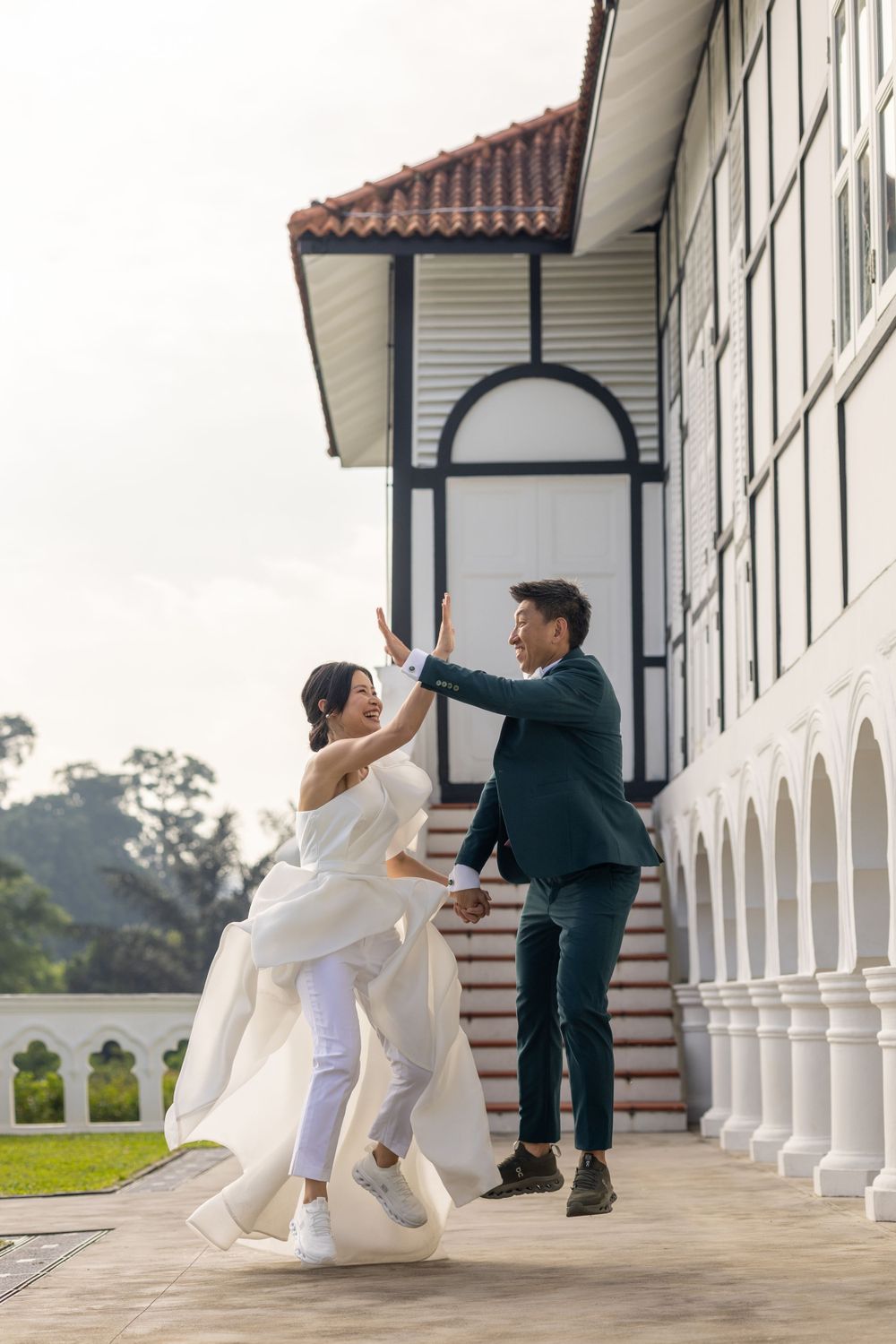 Couple in wedding attire dancing and celebrating on a colonial-style veranda.