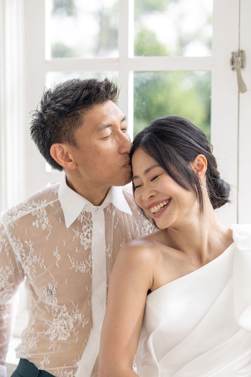 An intimate wedding portrait of a couple sharing a tender moment by a bright window.