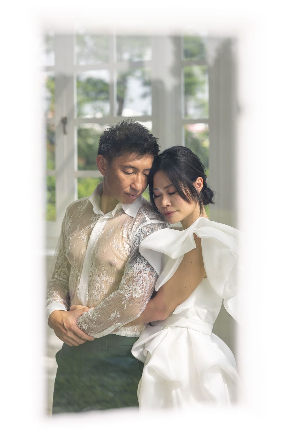 A dreamy wedding photo of a couple embracing in soft window light with vintage-style lace details.