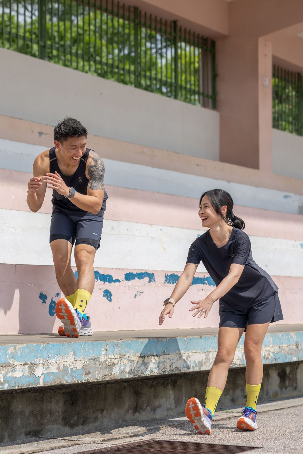 An athletic couple in dark workout clothes plays and jumps on concrete bleachers.