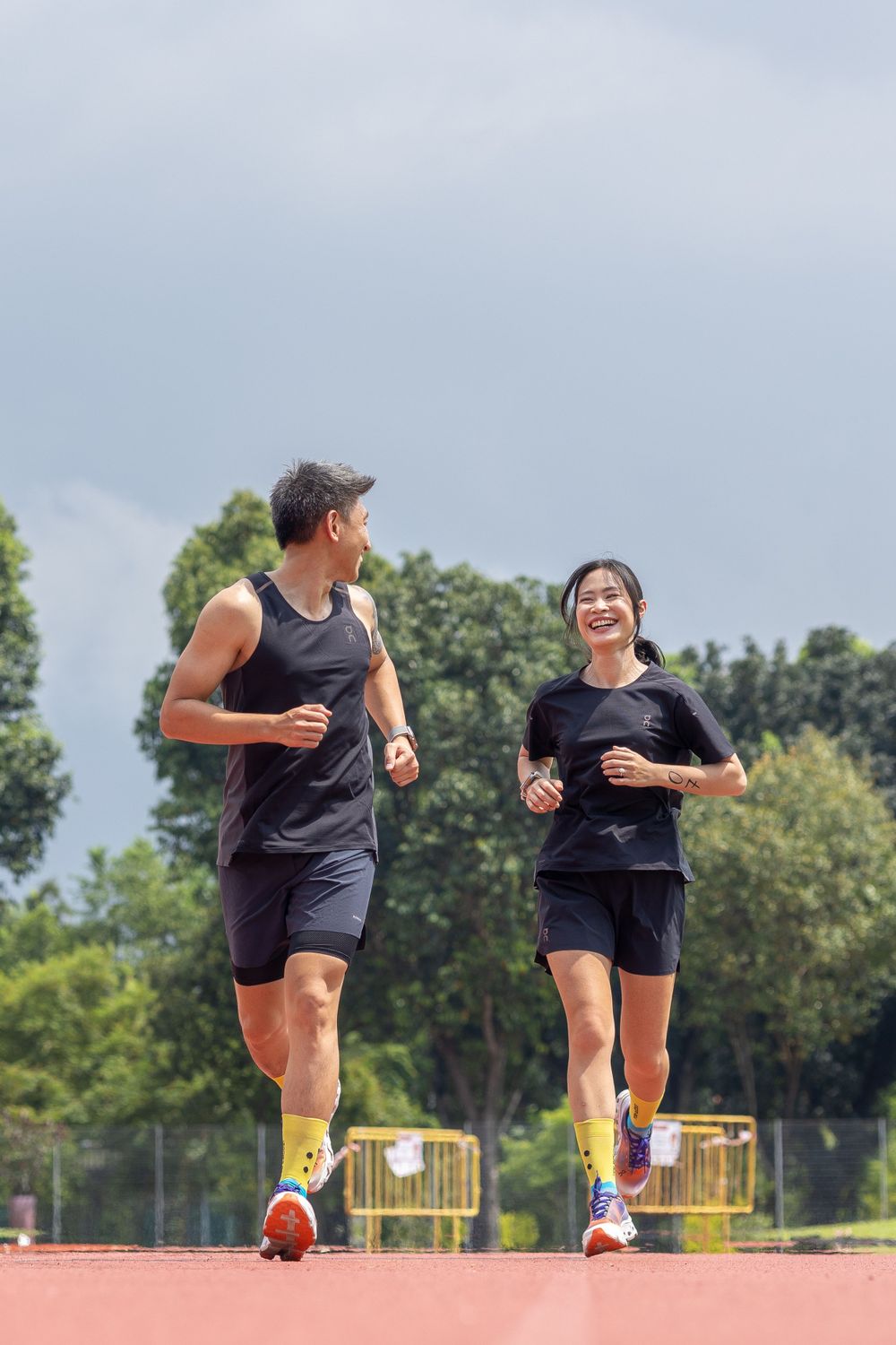 Two people jogging together on an outdoor track wearing matching black athletic outfits.