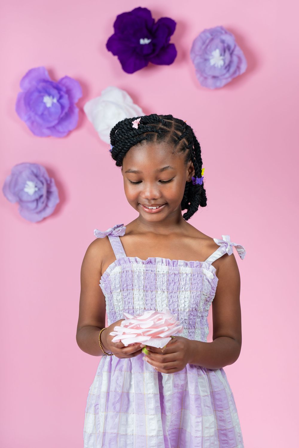 Child holding something while wearing white dress with purple floral decorations.