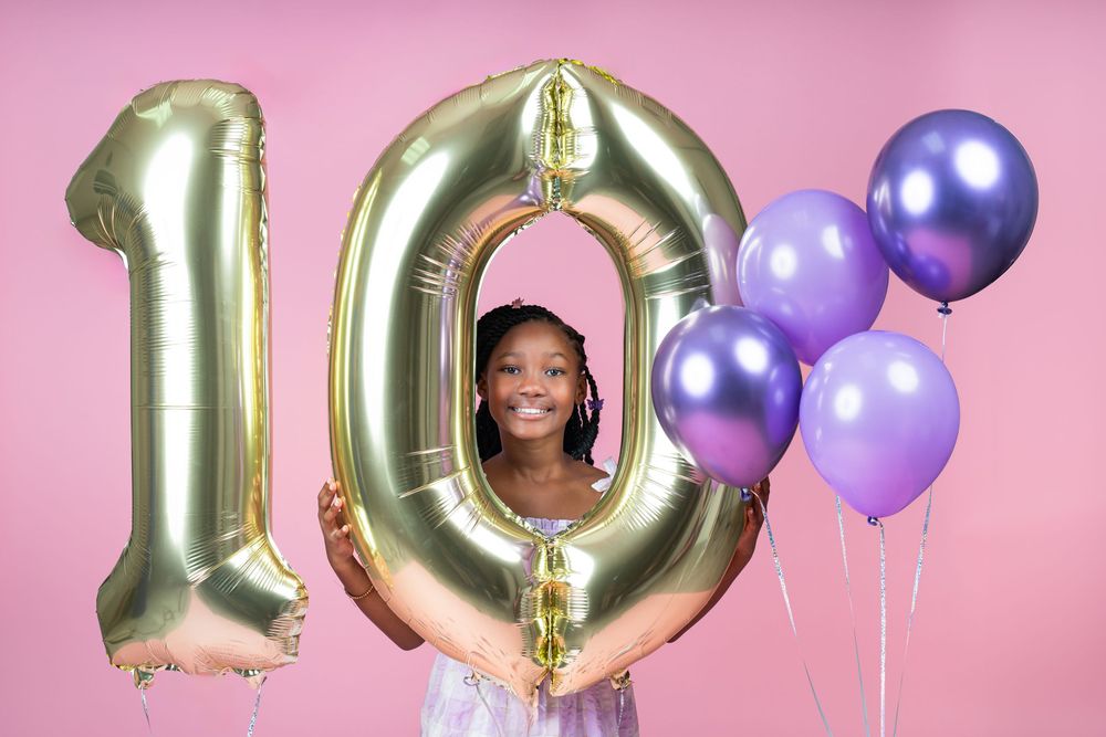 Gold number balloons and purple decorations against pink studio backdrop.