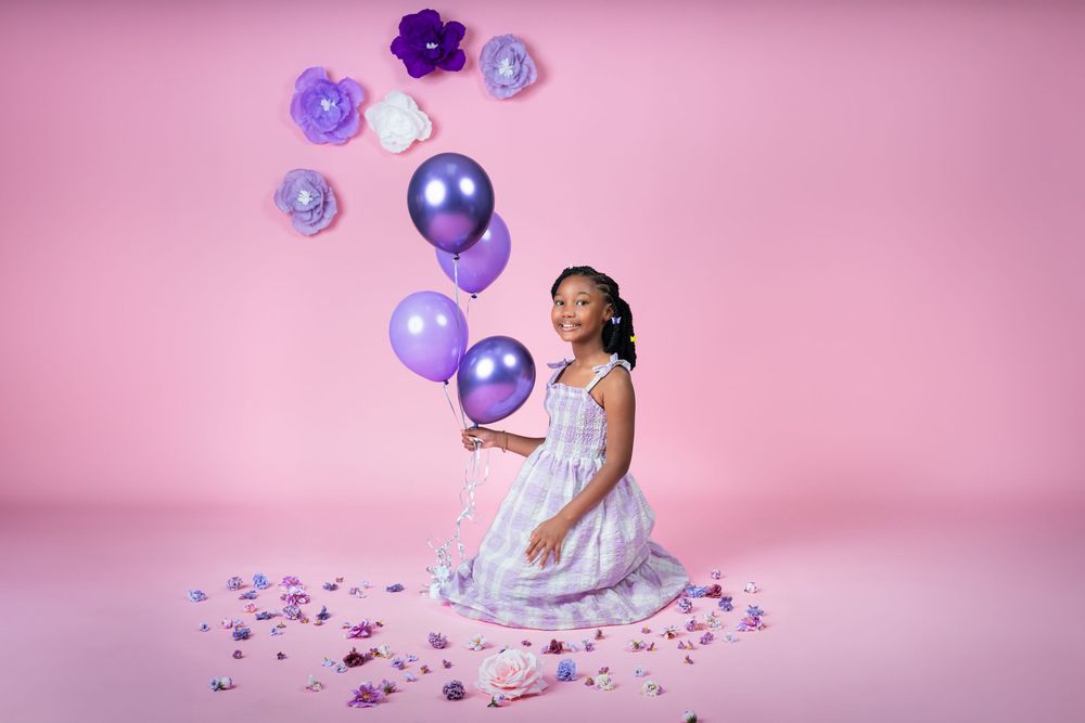 Purple balloons and floral decorations arranged on pink studio background.