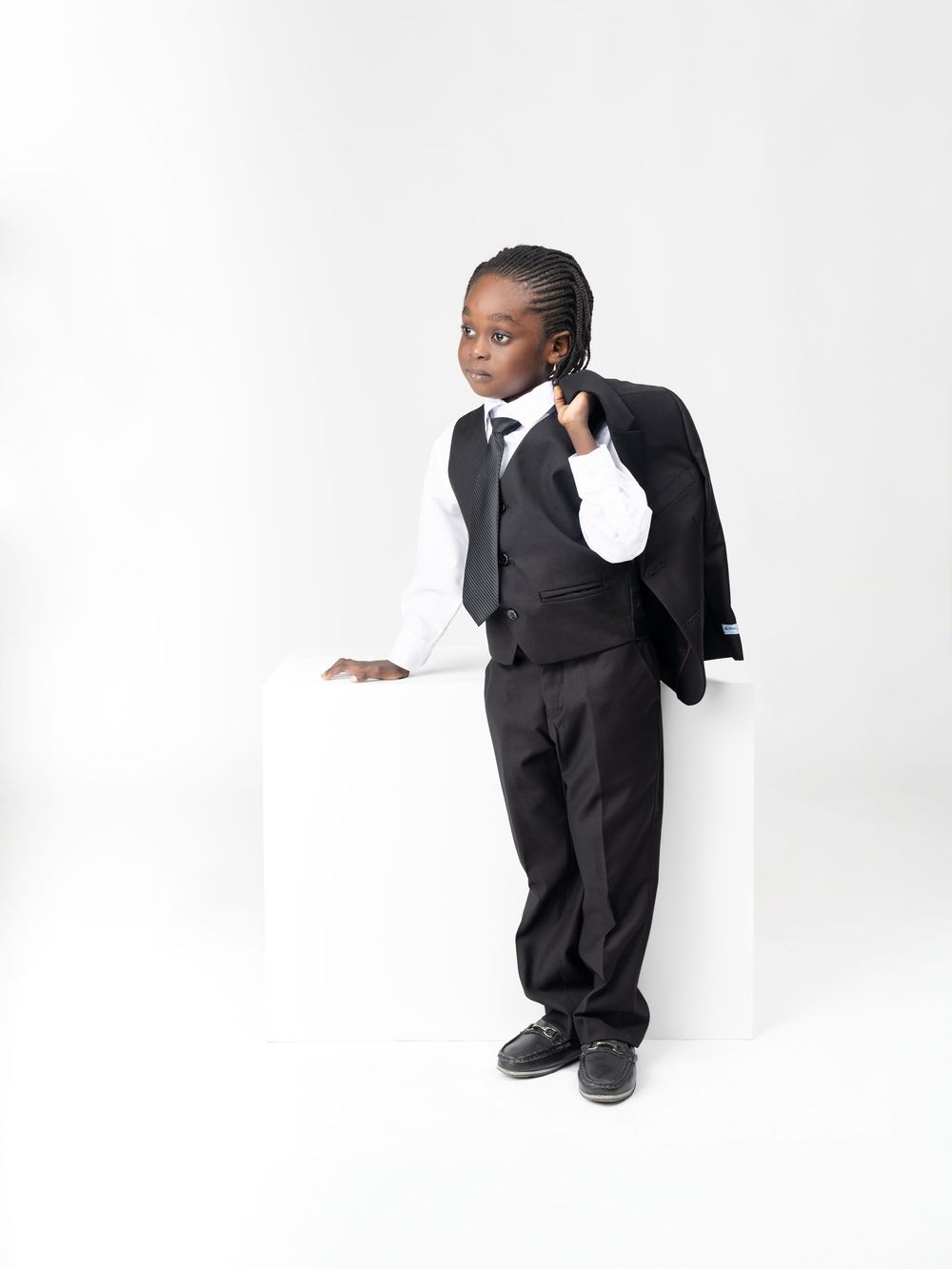 Stylish black suit photoshoot with creative poses against white backdrop.