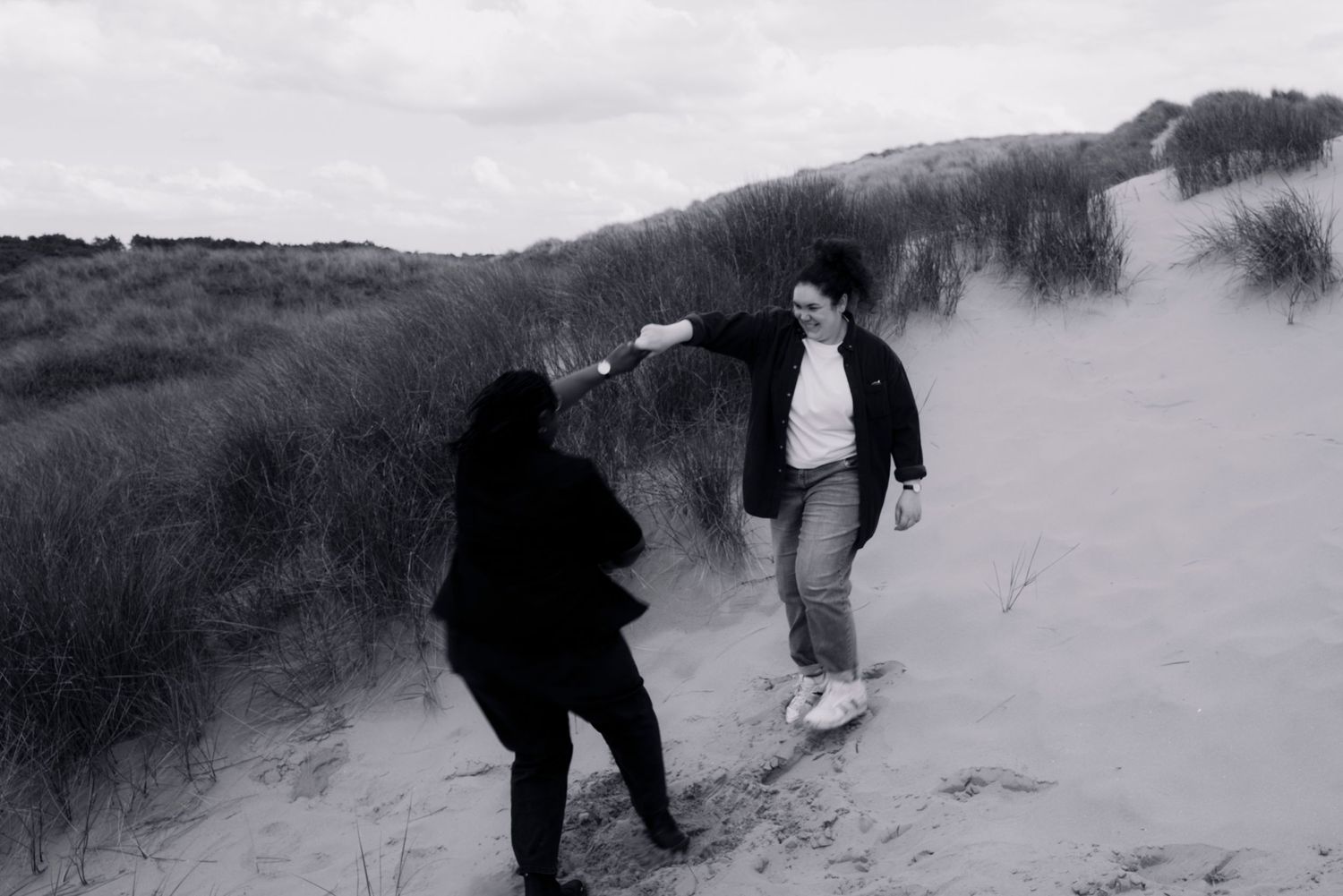 Candid black and white photo same sex engagement playing on sandy dunes—capturing joy, movement, and the beauty of carefree moments. lgbtq+