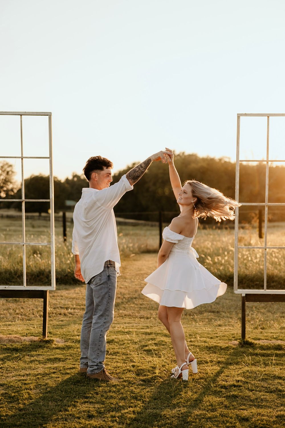 A couple dances together in a field at sunset with vintage window frames behind them creating a romantic scene.