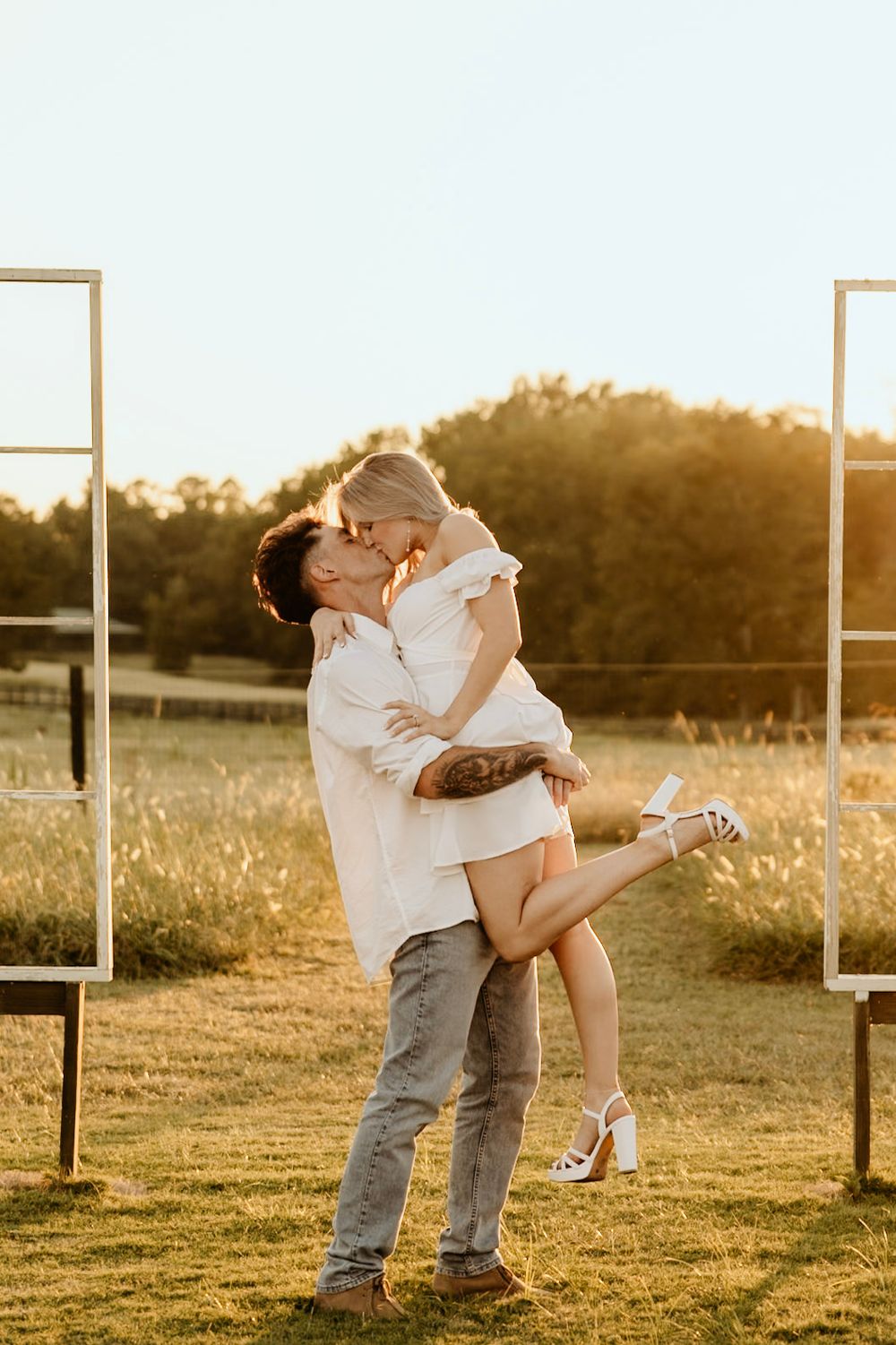 A romantic sunset embrace between two people in a golden field with white doors framing the scene.