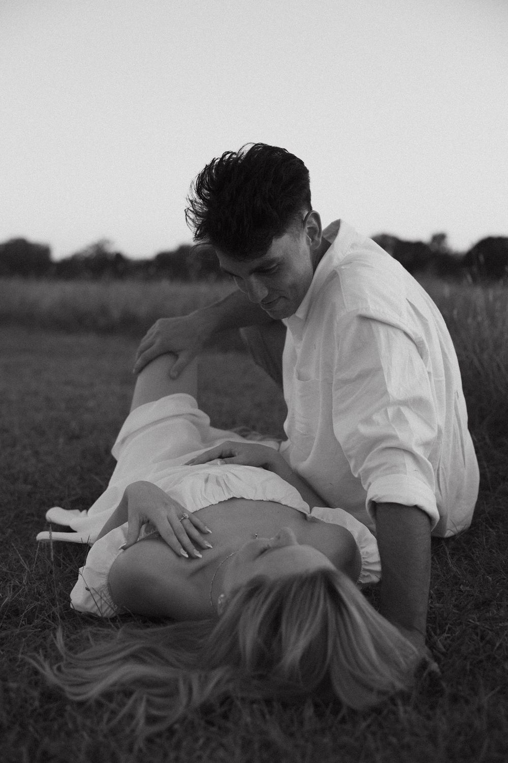A romantic black and white portrait of a couple sharing an intimate moment together in a grassy field.