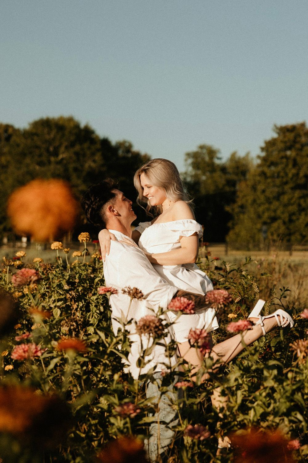 A romantic moment between two people sharing an embrace among blooming flowers at golden hour in a garden setting.