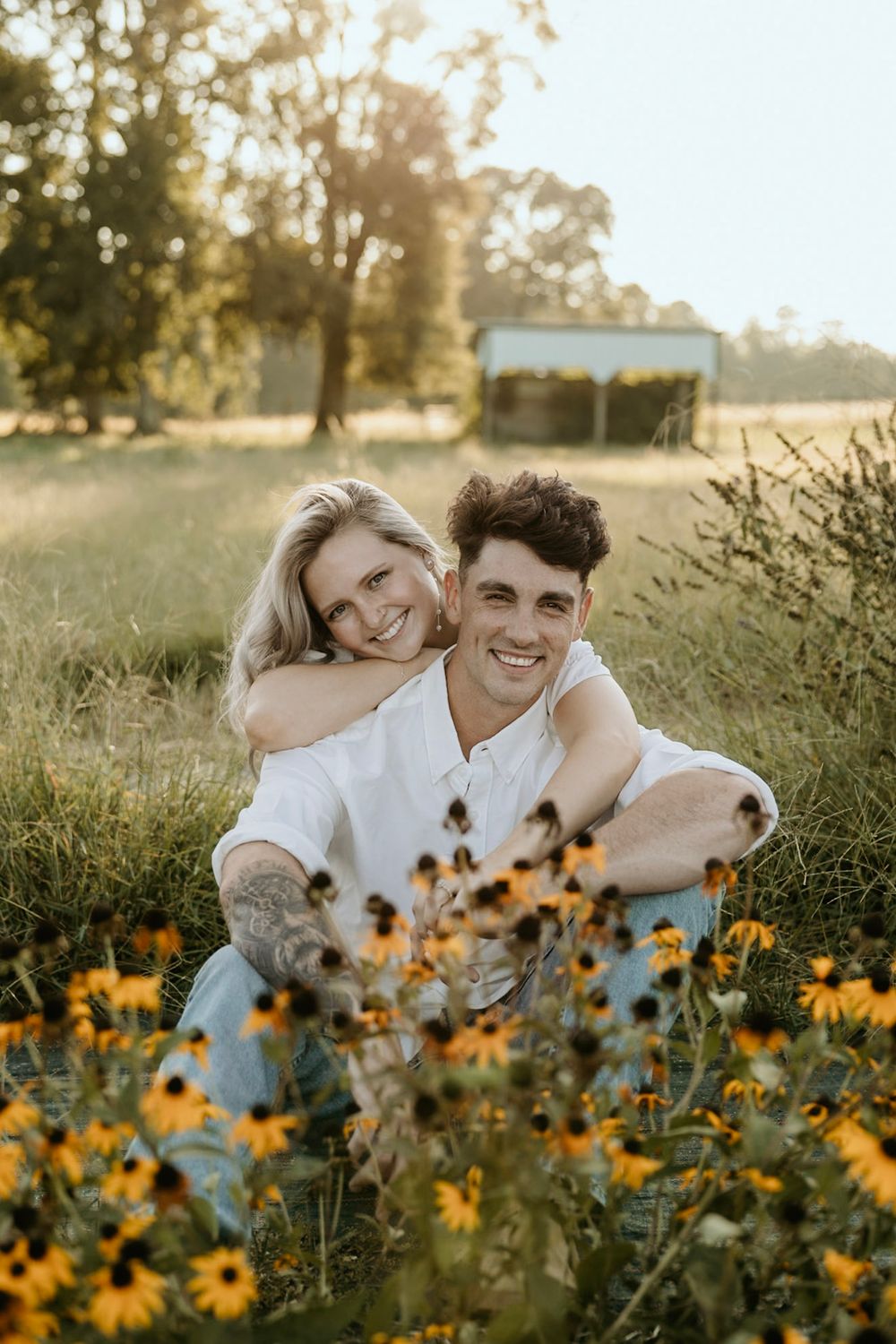 A romantic couple sitting among blooming yellow wildflowers in a sunny field at golden hour.