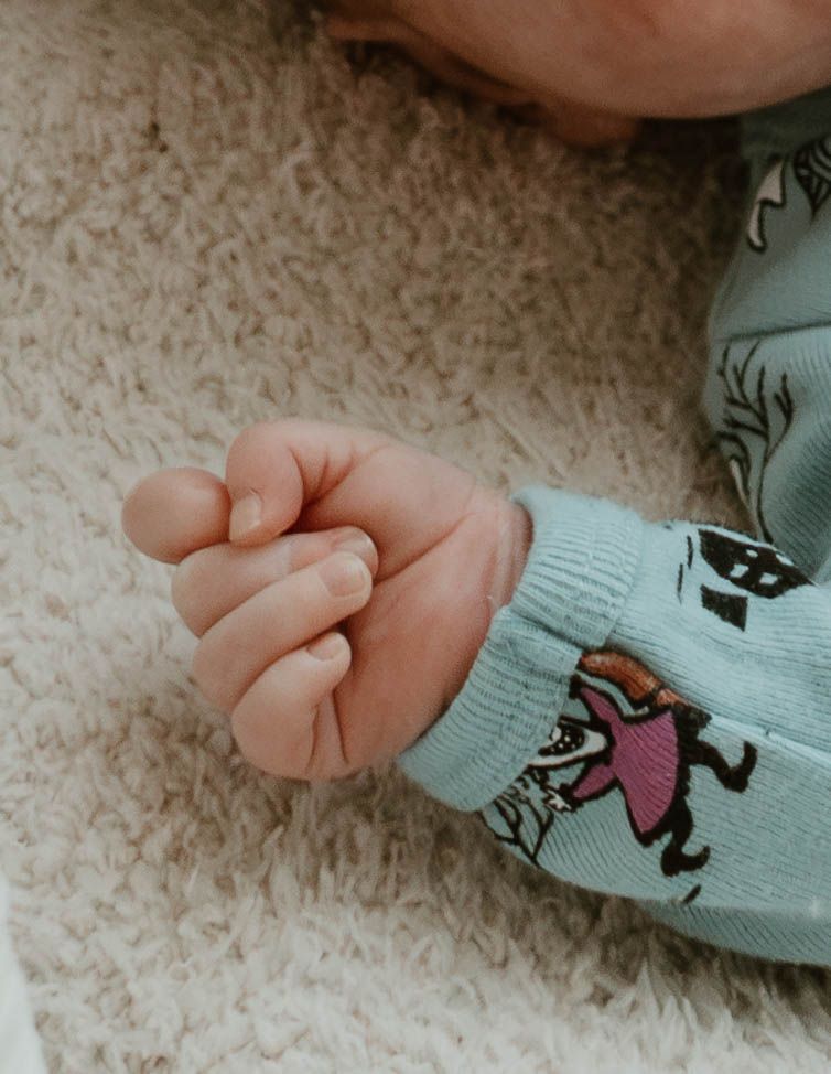Close-up of tiny baby hand wearing light blue patterned sleeve on carpet.