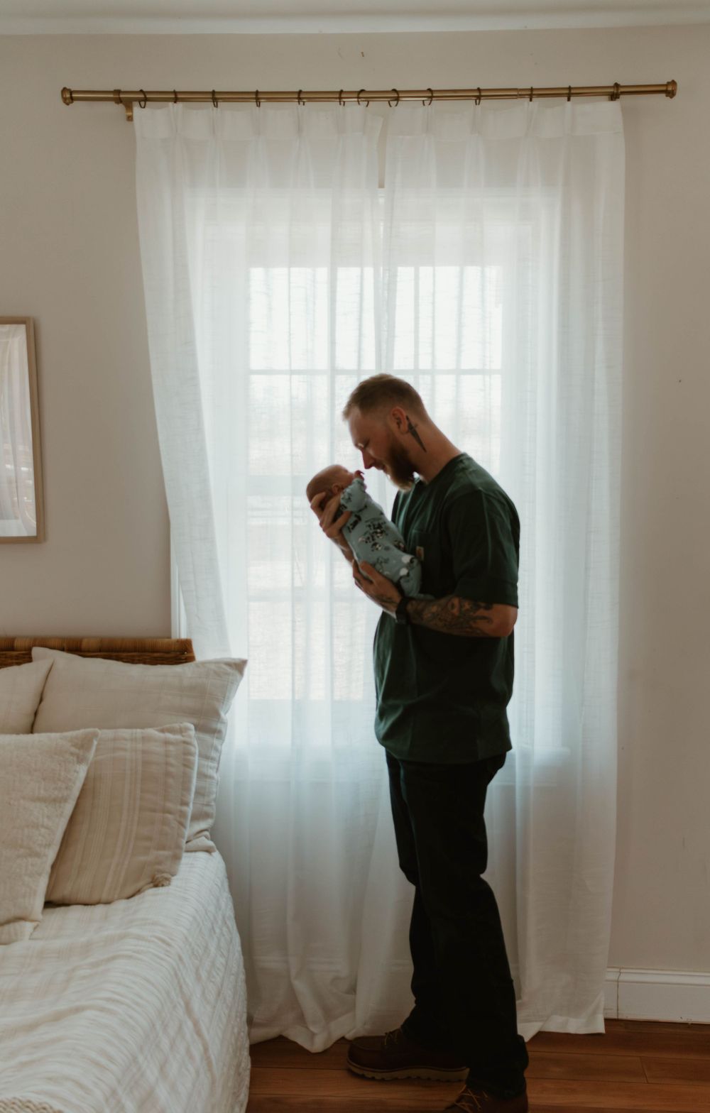 Silhouette of caregivers standing by window with sheer curtains in bedroom holding infant.