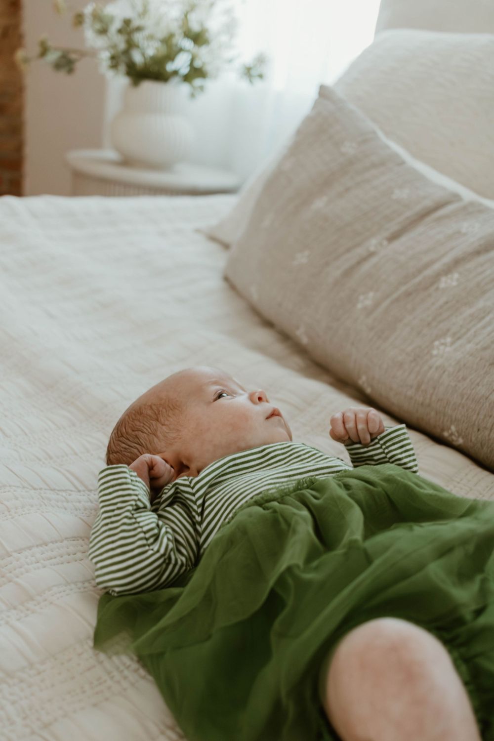 Baby in green striped outfit lying peacefully on white couch.