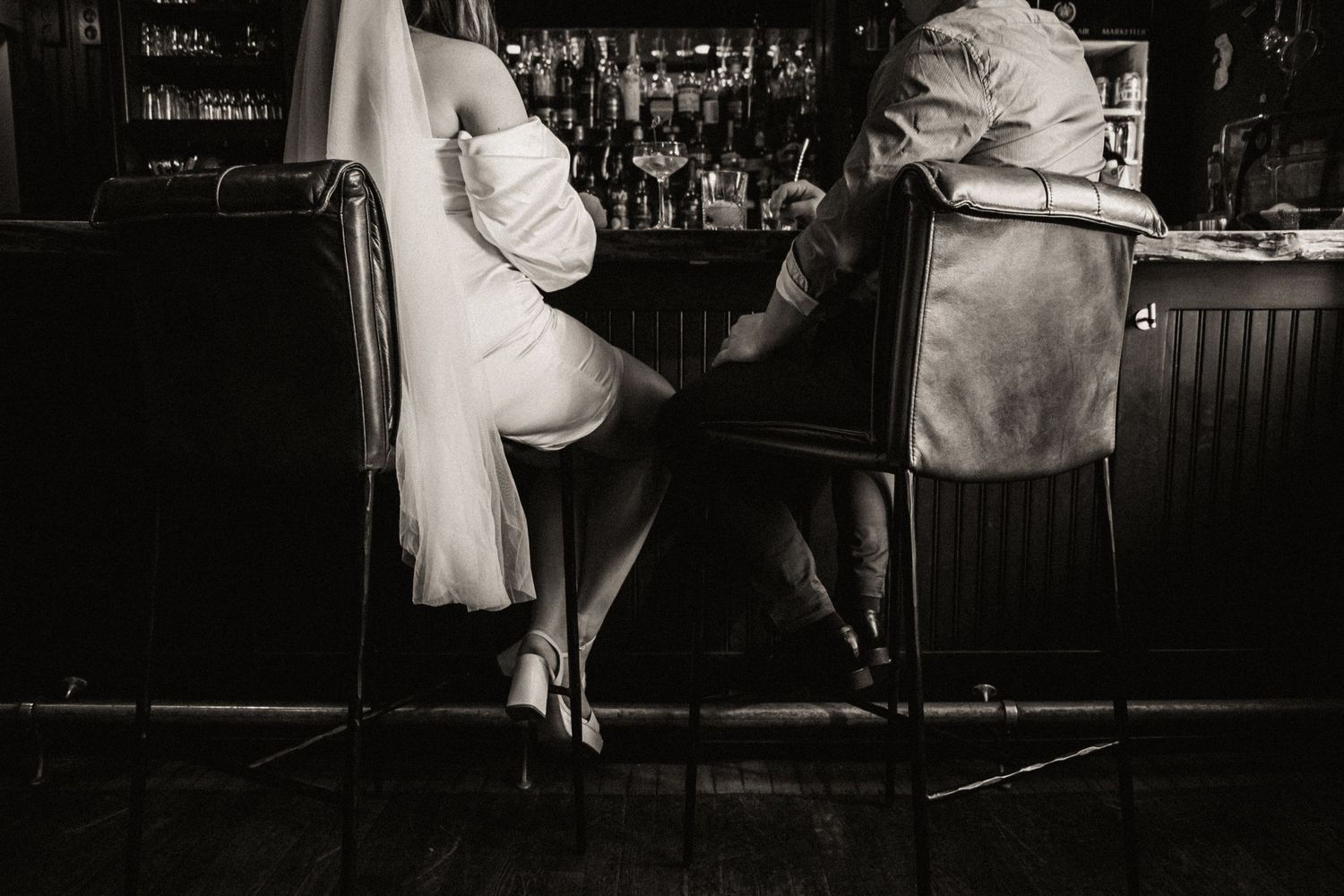 Black and white image of two people sitting at a vintage bar counter.
