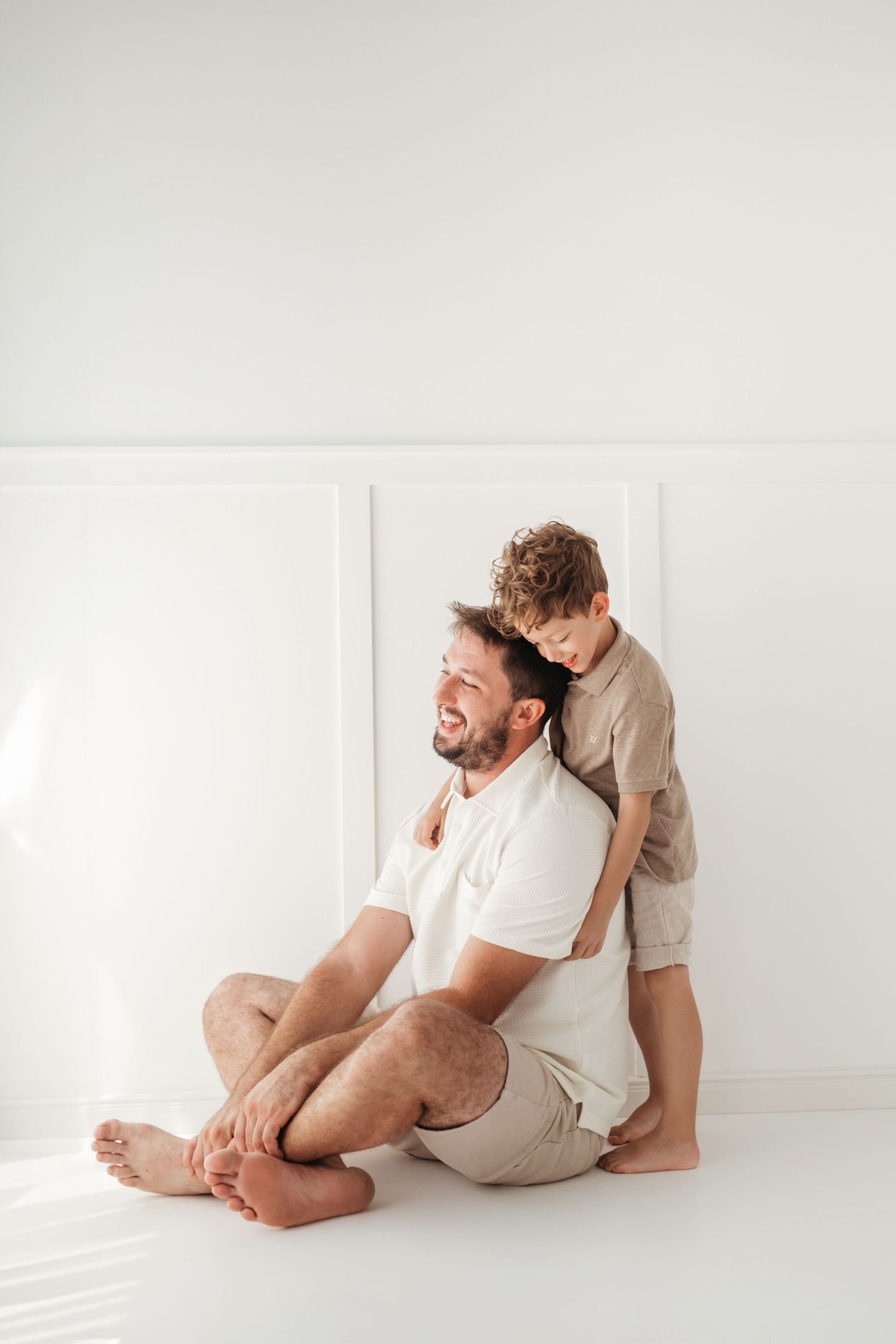 Two people sharing a tender moment while sitting on a white floor against a minimalist white wall background.