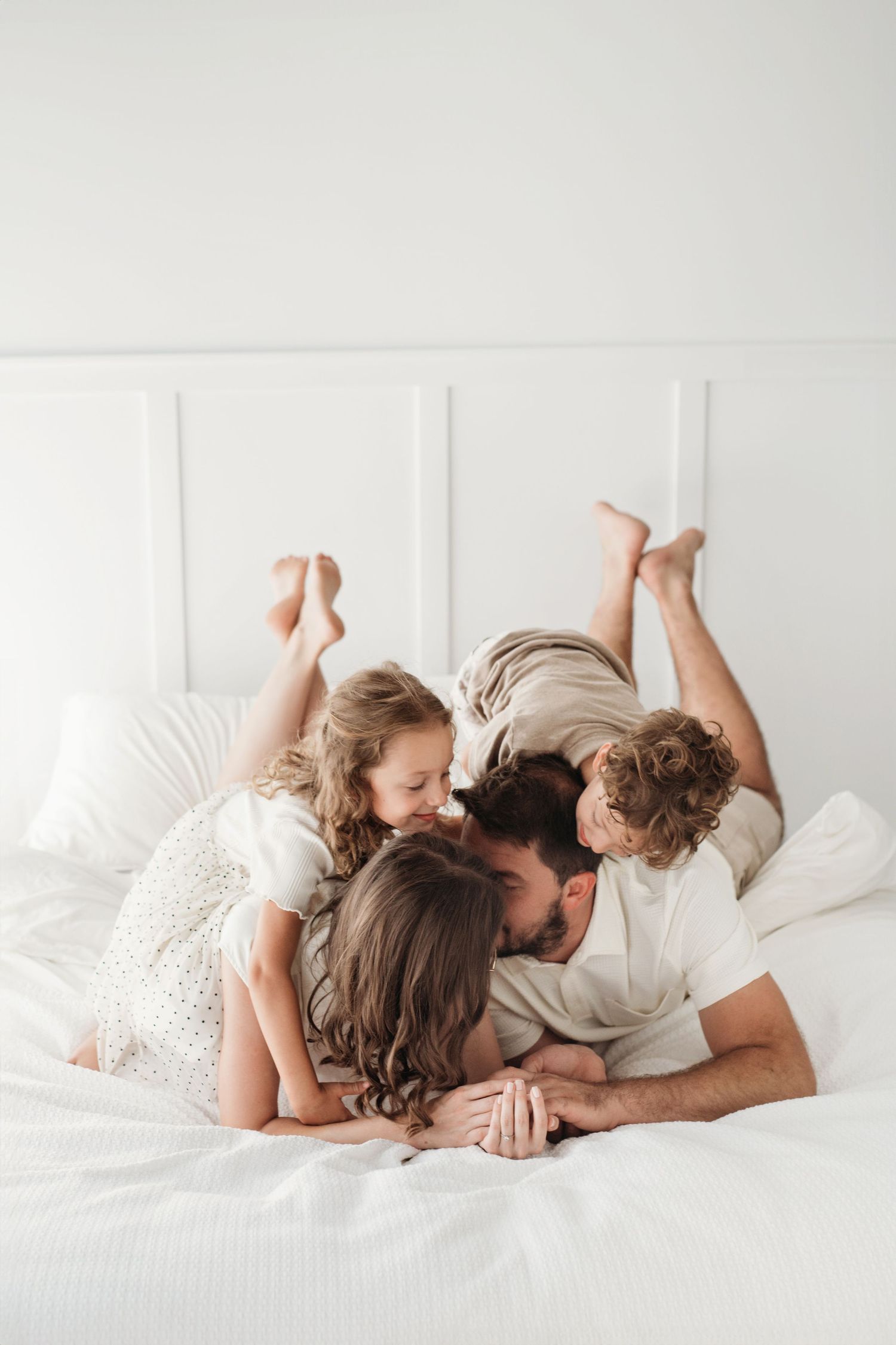 A tender family moment as they cuddle together in a cozy white bed, sharing laughter and intimacy.