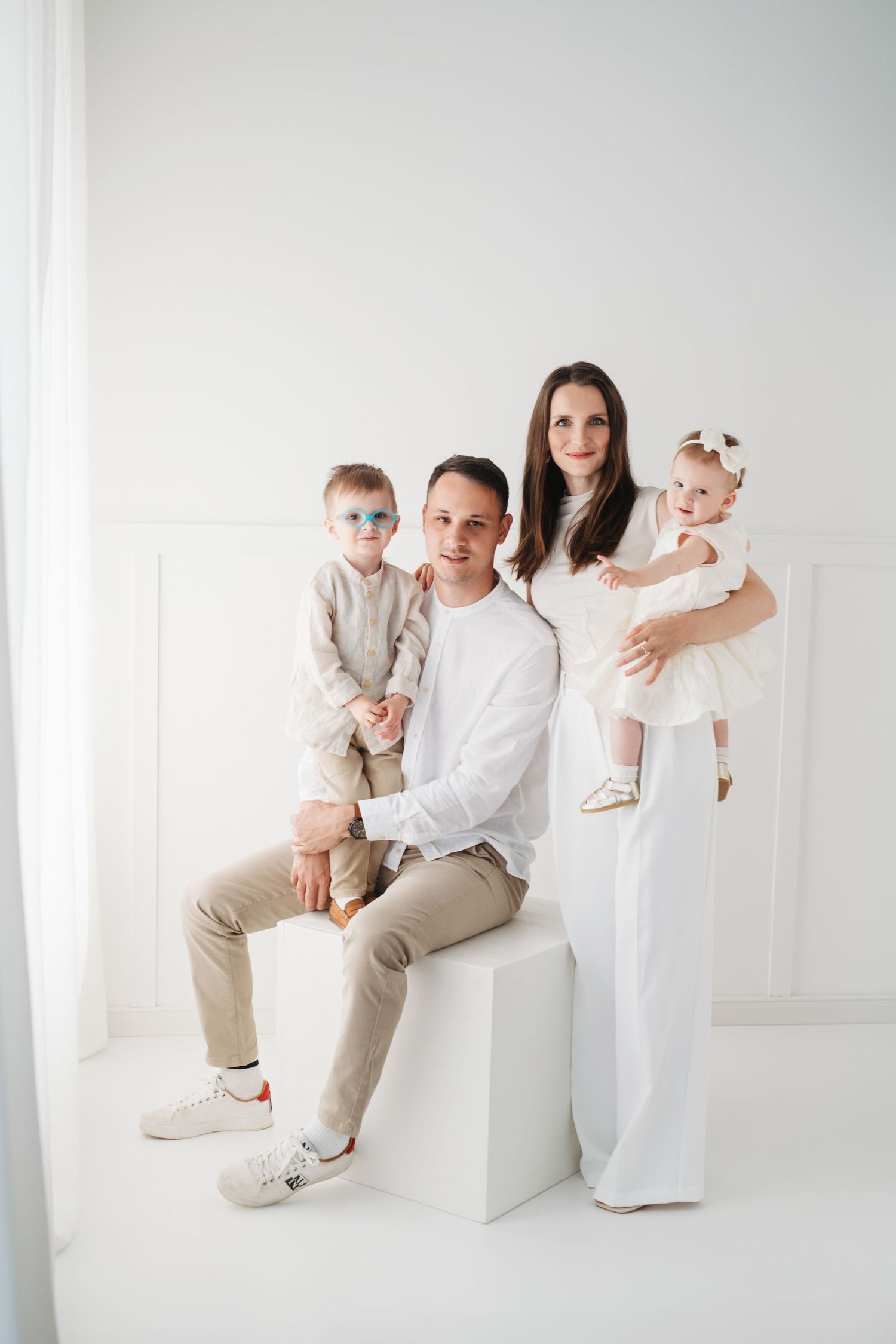 Family portrait in minimalist white studio with parents and children wearing coordinated neutral outfits.