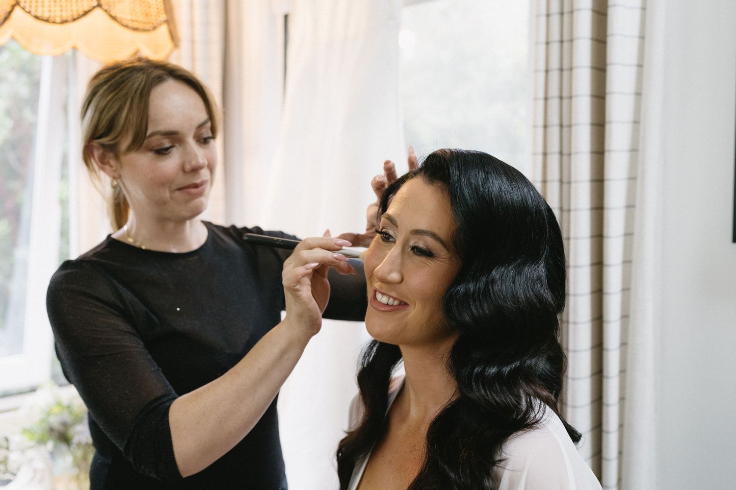 A makeup application session taking place in a bright, natural-lit room.
