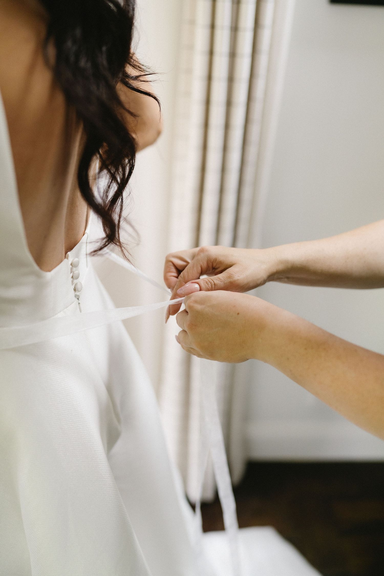 Hands adjusting the back of a white wedding dress during preparation.