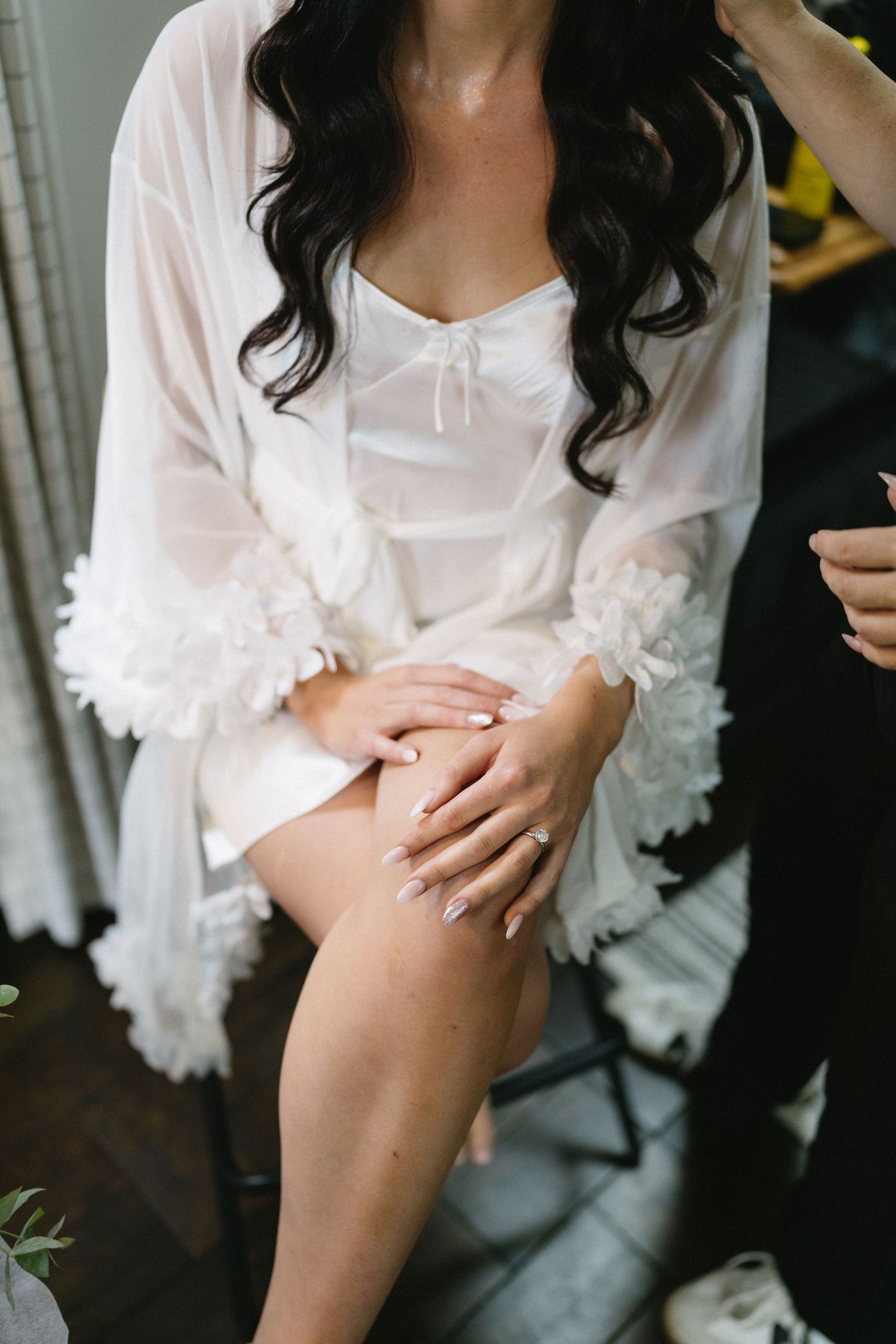 A person in a white lace robe sits with hands resting on their knee.