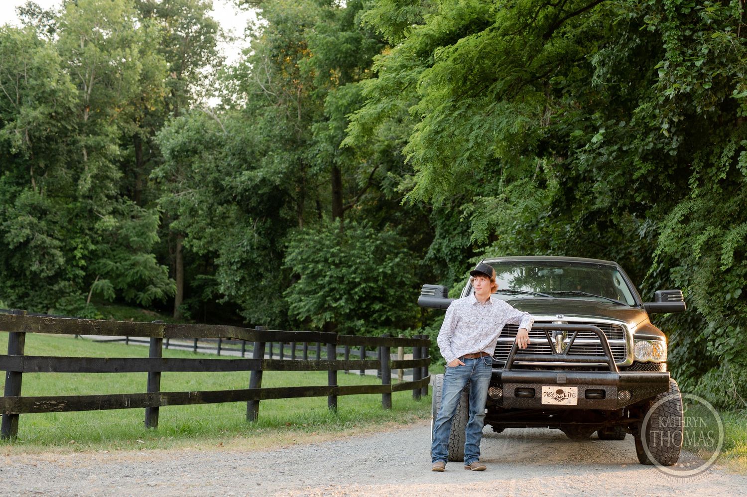 A black lifted pickup truck parked on a gravel road beside wooden fencing.