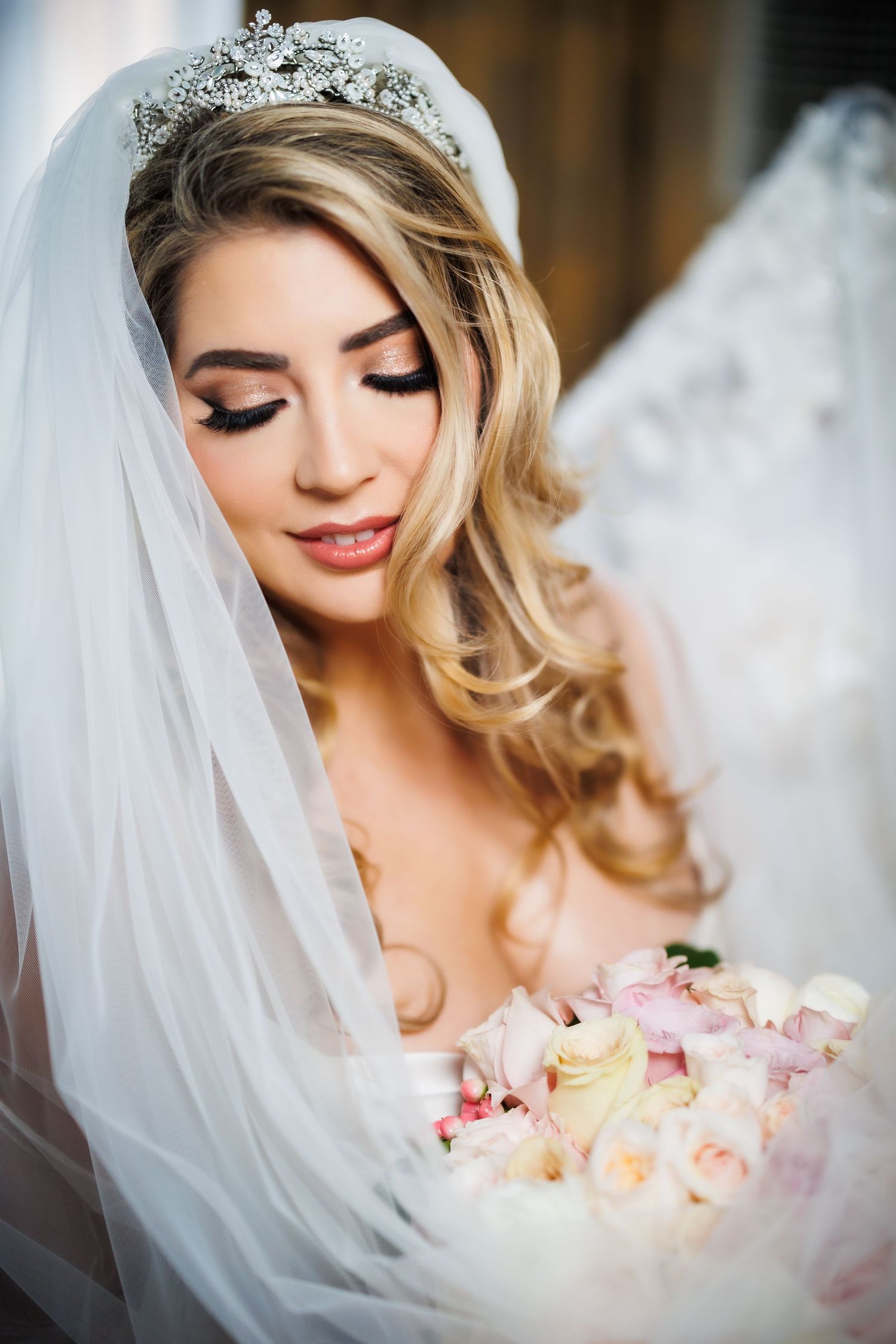 Elegant bridal portrait showing delicate veil, crystal headpiece, soft wavy blonde hair and romantic pastel bouquet.