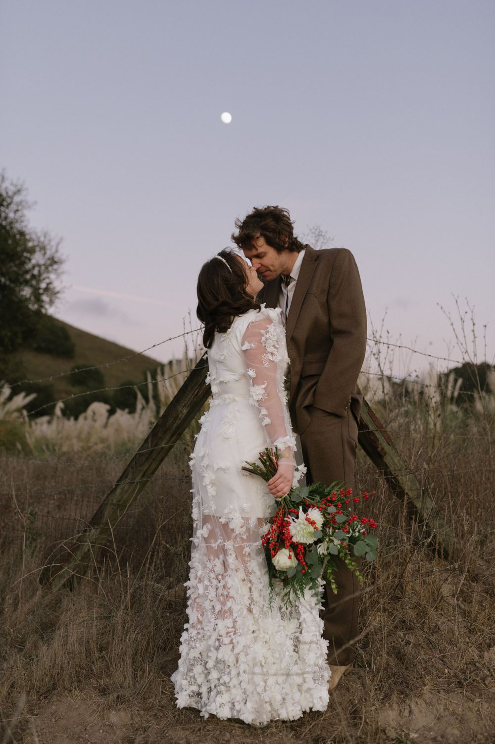 A romantic moonlit wedding portrait with the bride holding a red and white floral bouquet.